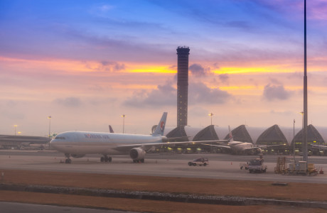 In der Dämmerung steht im Vordergrund eine Maschine von Korean Air auf dem Rollfeld, im Hintergrund ragt der Airport Tower am Flughafen Bangkok-Suvarnabhumi in die Luft.