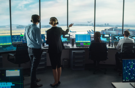 In einem Flughafen-Tower beobachten mehrere Personen den Start eines Flugzeugs.