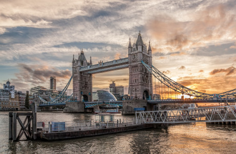 Die Tower Bridge in London vor einem dramatischen Sonnenaufgang, im Vordergrund ist ein Steg zu sehen.